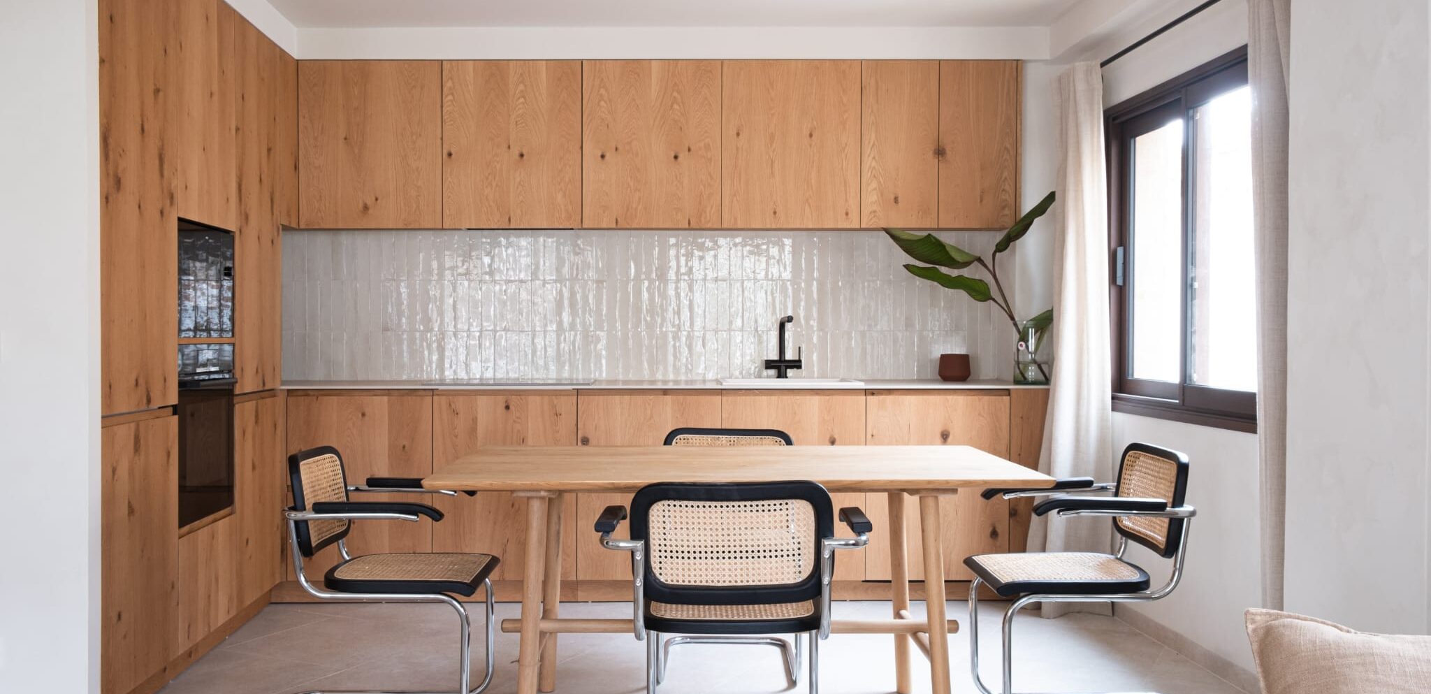Cocina con mobiliario de madera, grifería negra y comedor con sillas estilo vintage